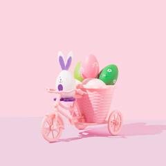 Bunny rides a pastel pink bicycle and transports colorful Easter eggs. Creative springtime holiday concept. Frontal view.	