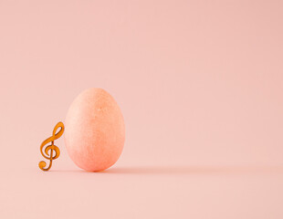 Composition of pastel orange egg and wooden treble clef. Minimal holiday Easter musical concept....