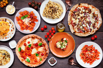 Fototapeta na wymiar Delicious Italian food table scene. Selection of pizzas, pastas, gnocchi, risotto and bruschetta. Top view on a dark wood background.