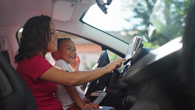 Caring parent teaching her son how to drive car. Mother plays with little son in the car. Toddler pretending to drive
