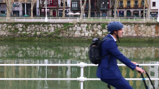 Businessman Commuting Sustainably with Electric Folding Bike near City River (4K video)