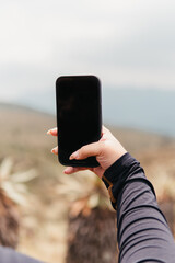 Hand holding a smartphone with a blank screen against a natural background, poised to take a photo