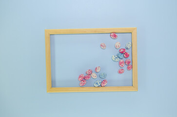 Easter wooden frame with colorful egg shaped candies and copy space, flat lay on the blue background.