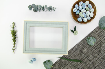 Blue easter eggs on white background with gray tablecloth with dried foliage and light blue wooden frame - easter composition with copy space, flatlay
