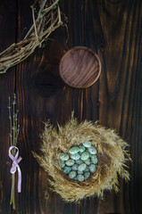 Easter composition. Green eggs in nest on dark vintage wooden background with wooden plate and willow wreath. Copy space.