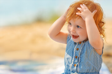 Portrait of redhair baby sitting in the sea water, summer activity. Surprised girl.