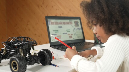 African girl writing car model structure while laptop display code. Smart student working by using...