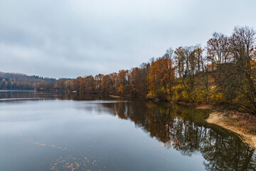 Beautiful view to big lake with silent water and reflecting trees and cloudy sky seen from bridge at rainy morning