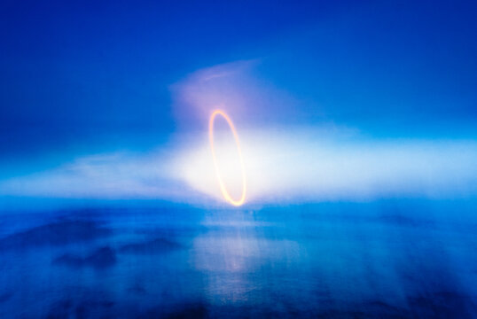 An abstract motion blurred light painting of the setting sun in a blue sky over the ocean along the California coast