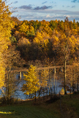 Beautiful mountain landscape full of golden and green trees at fall and long steel and wood bridge at the center of big lake at down of the hill