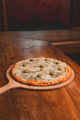 Cheese pizza with olives on a wooden bar table.