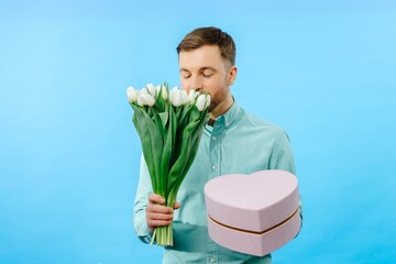 Man holding bouquet of tulips and gift box, looking at camera isolated on blue background. Celebration concept