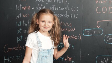 Happy smart caucasian girl smiling at camera while waving hands to camera.while standing at board...