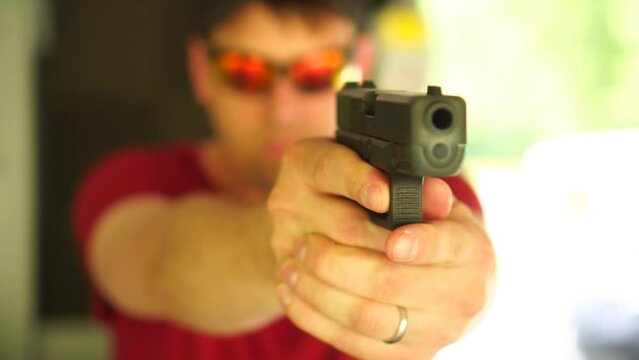 Blurry man in sunglasses holding a pistol at a gun range