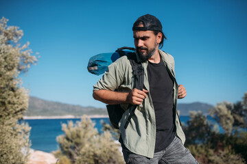 A male tourist with a large backpack and equipment on a mountain trail among the trees.