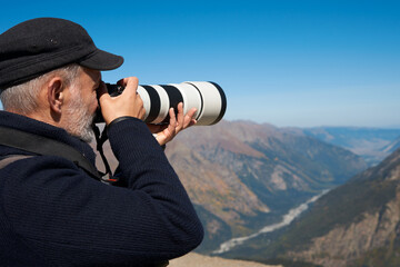 An adult man with a camera with a long-focus lens on the background of a high-mountainous...