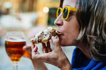 side close-up, of a woman wearing yellow glasses, eating a slice of homemade pizza, made with veal...