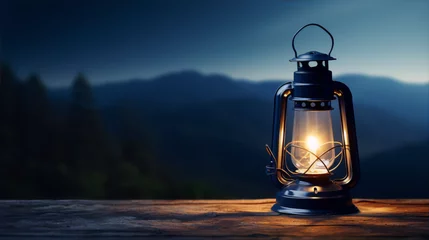 Fotobehang A glowing lantern on a wooden table with a blurred mountain landscape and dark blue night sky in the background. © zhor