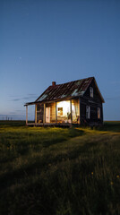 Small wooden house in the middle of a grass field at night with a starry sky and light coming out of the windows.
