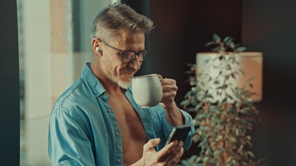Man drinking morning coffee checking phone at home - 754537496