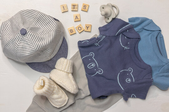 It's a boy words on flat lay of blue baby boy clothes, cap and booties on white background with copy space for gender reveal or baby boy announcement