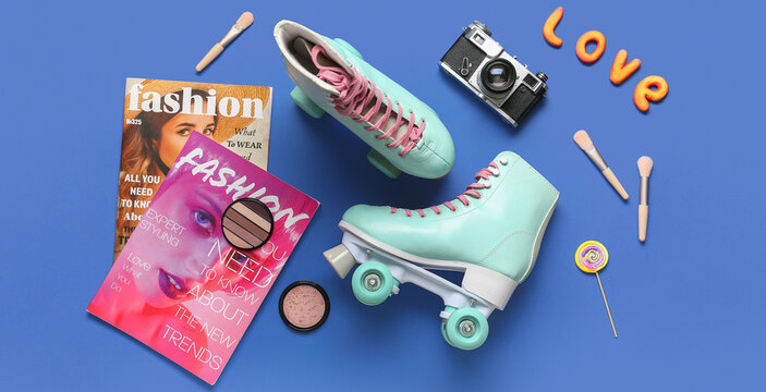 Composition with pair of vintage roller skates, photo camera, magazines and cosmetic products on blue background