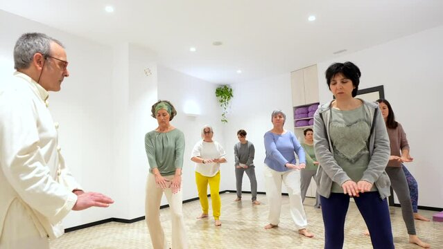 Qi gong male instructor leading a wi gong session class with mature and adult caucasian women