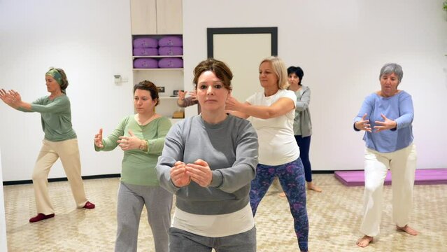 Group of mature adult and caucasian sportive women opening arms during qi gong class