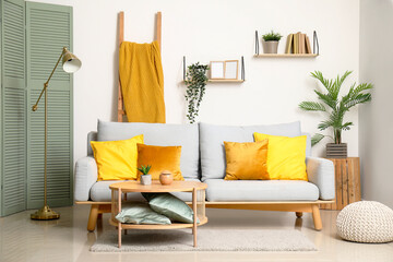 Stylish interior of living room with soft sofa, pillows, houseplant and table