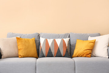 Stylish grey sofa with pillows near beige wall