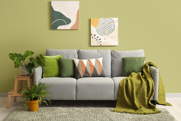 Stylish grey sofa with pillows, paintings and houseplants near green wall