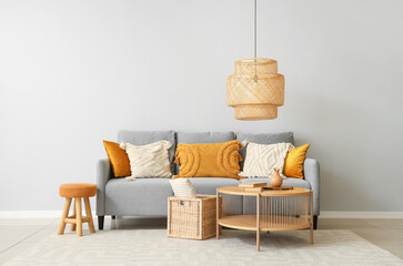 Stylish grey sofa with pillows, coffee table and wicker basket near grey wall - obrazy, fototapety, plakaty