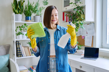 Young woman cleaning house, wearing gloves with cleaning spray and rag - obrazy, fototapety, plakaty