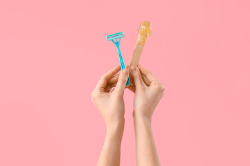 Female hands holding spatula with sugaring paste and razor on pink background