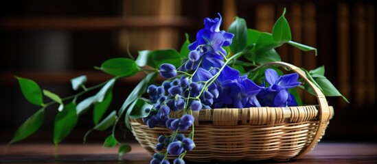 A bamboo basket filled with bright blue pea flowers and lush green leaves sits on a wooden table.