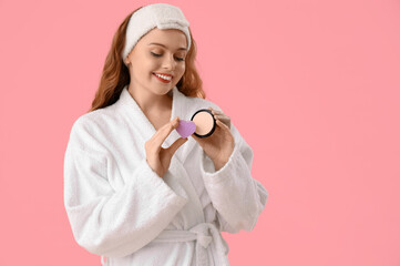 Beautiful young woman in bath headband with heart-shaped sponge and makeup powder on pink background