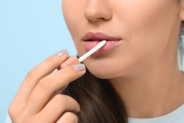 Young woman applying lipgloss on color background, closeup