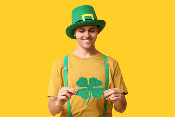 Happy young man in leprechaun's hat and with clover on yellow background. St. Patrick's Day