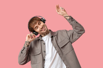 Young tattooed man with headphones dancing against pink background