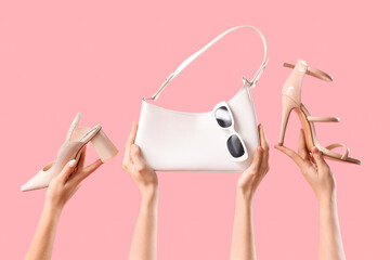 Female hands with stylish women's bag, sunglasses and high heels on pink background