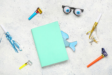 Notebook with paper fish, funny glasses and party whistles on light grunge background. April Fool Day