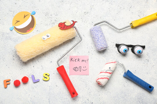 Paint rollers with text FOOLS, funny glasses and sticky note on light grunge background