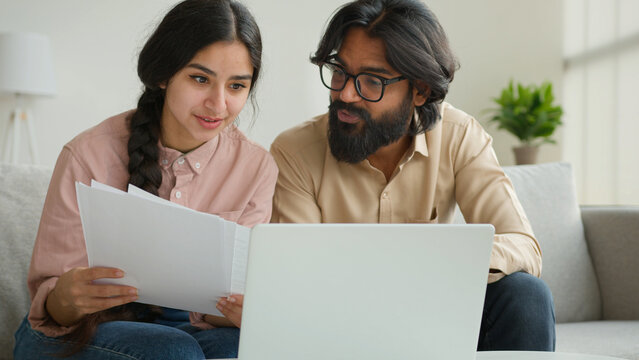 Arabian couple homeowners read tenancy papers at home paying domestic bills taxes online on laptop multiethnic woman and man planning budget talking discuss documents loan payments bank house mortgage
