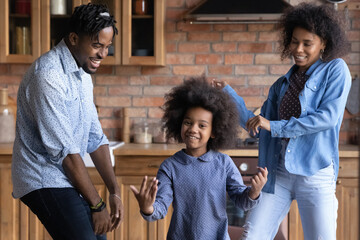 Cheerful lively 35s African ethnicity couple and their preschool cute daughter dancing in cozy...