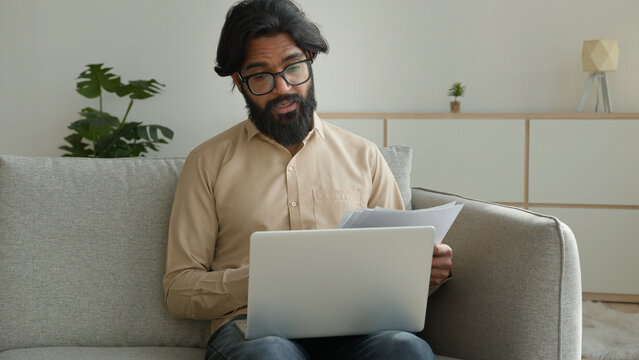 Internet tutor teacher in eyeglasses muslim man guy male Indian Arabian businessman talk video meeting on laptop webcam business conference online in quarantine discuss papers documents solve problem