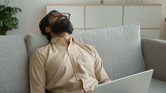 Tired exhausted freelancer working with laptop at home overworked Arabian muslim man fall asleep on couch sick weary sleeping Indian businessman lean on sofa exhaustion fatigue need break rest relax