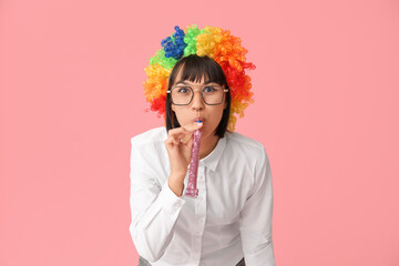 Funny young businesswoman with party blower on pink background. Fool's day