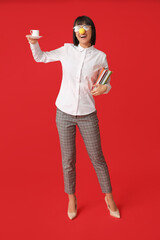 Funny young businesswoman with cup of coffee on red background. Fool's day