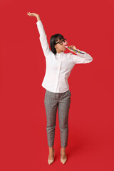 Funny young businesswoman with party blower on red background. Fool's day