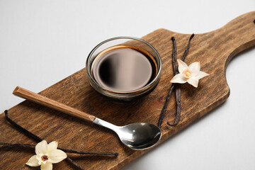 Vanilla extract in bowl with vanilla pods and flowers on cutting board, pink background